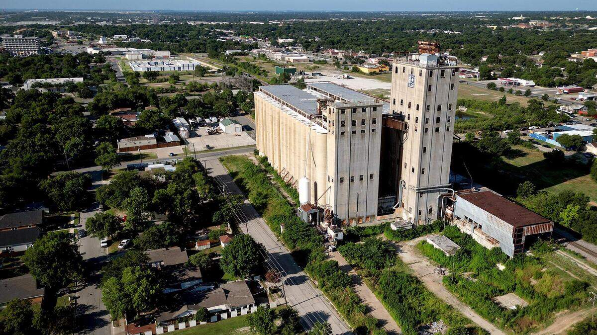 A drone photo of a very tall large building surrounded by one story homes and trees.